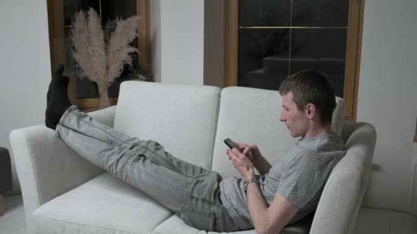 Mann liegt auf Couch im Smartphone-Chat, SMS per Handy. Zuhause bleiben — Stockvideo