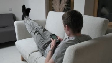 Adam kanepede uzanıp akıllı telefondan sohbet ediyor, cep telefonuyla mesajlaşıyor. Evde kal.