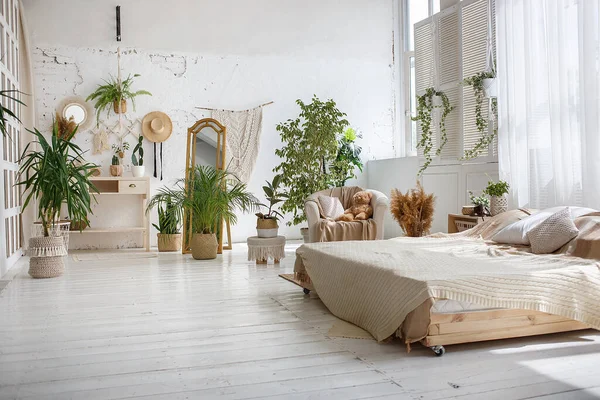 Stylish bright loft cozy room with double bed, armchair, green plants, mirror, white brick walls and wooden floor.