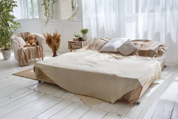 Стильный светлый лофт уютный номер с двуспальной кроватью, креслом, зелеными растениями, шторами, белыми стенами и деревянным полом . — стоковое фото