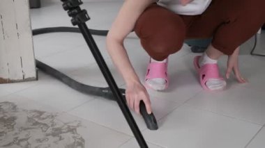 Tanımlanamayan pembe terlikli kız elektrikli süpürgeyle yerleri süpürüyor.