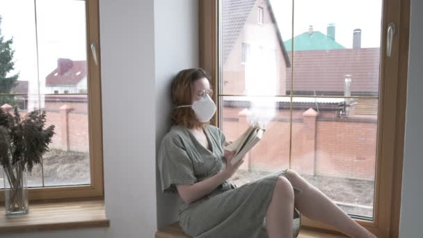 Jong meisje in beschermende masker, bril zit op vensterbank, leest gedichten boek — Stockvideo