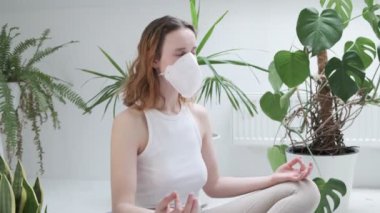 Koruyucu maskeli bir kız Lotus pozunda meditasyon yapıyor.