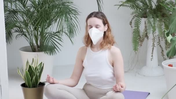 Concepto de estancia en casa: chica en ropa deportiva, máscara protectora meditando en habitación luminosa — Vídeos de Stock