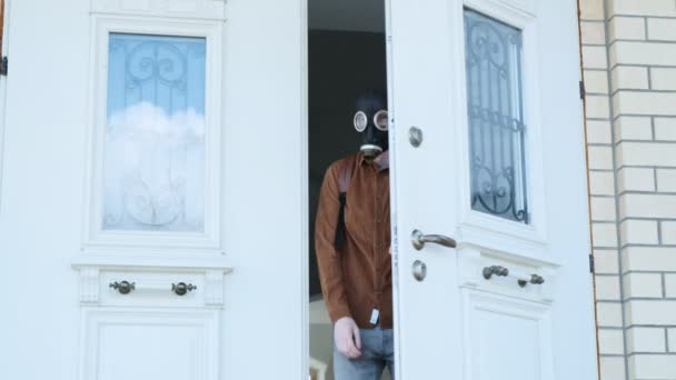 Døren åbnes, unge mand i gasmaske kommer ud af huset, ser sig omkring og blade – Stock-video