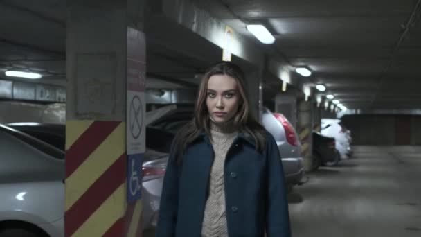 Stijlvol attent aziatisch meisje in jas wandelingen op ondergrondse parkeren langs auto 's — Stockvideo