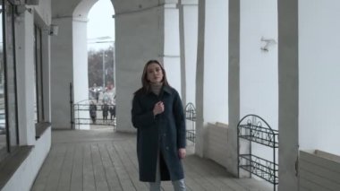asian pretty girl in blue coat stands alone on veranda with white stone columns