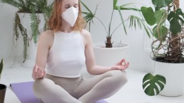 Koruyucu maske takan kız Lotus pozu verip meditasyon yapıyor. ev konsepti