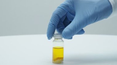 Bilim adamları mavi eldivenleriyle cam şişeyi sallıyor. Klinik aşısı