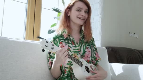 Karantän fritid: ung flicka i blommig skjorta strumpa ukulele på solig dag — Stockvideo