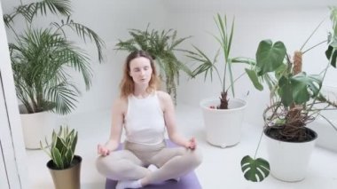 Spor kıyafetleri giyen bir kız Lotus pozisyonunda oturur. Gözleri kapalı, meditasyondan zevk alır.