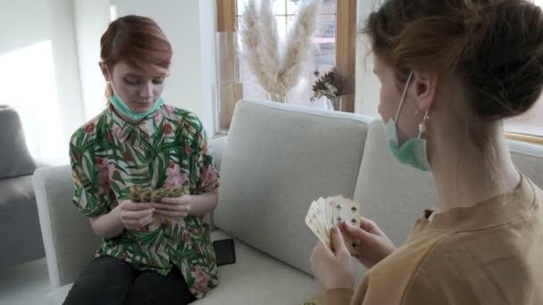 Przyjaciele lub siostry rozmawiają, grają w pokera w domu, bawią się. dziewczyny grają w karty na kanapie — Wideo stockowe
