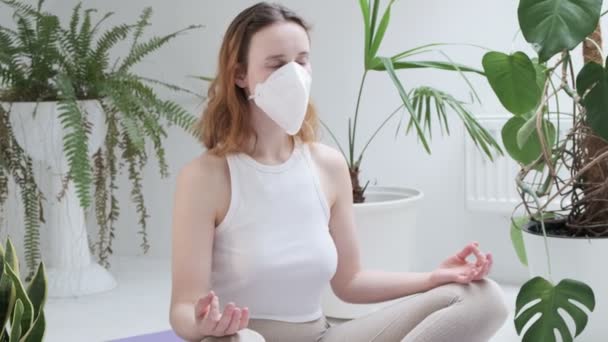 Blijf thuis concept: meisje met beschermende masker zit in lotus poseren mediteren — Stockvideo