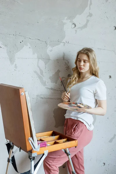 Pobyt doma: mladá dívka se štětcem a paletou stojící u stojanu kresba — Stock fotografie