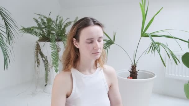 Дівчина в спортивному одязі сидить в позі лотоса з закритими очима насолоджується медитацією — стокове відео