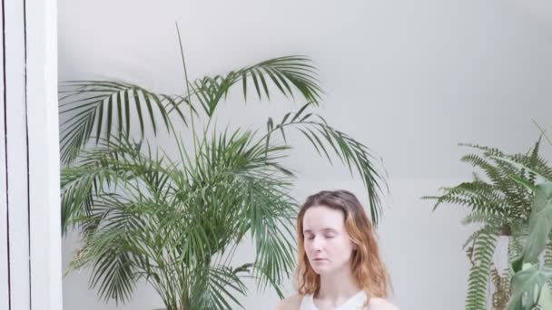 Chica con ropa deportiva se sienta en pose de loto con los ojos cerrados disfruta de la meditación — Vídeos de Stock