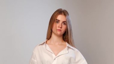Burnunda piercing olan beyaz bir kadın ayakta, göz kırpıyor ve kameraya bakıyor.