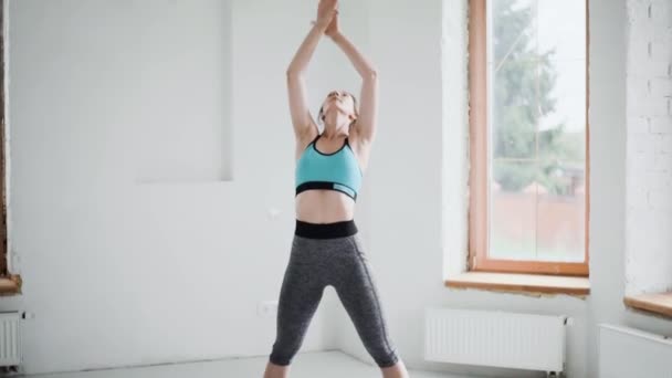 Joven chica morena deportiva en ropa deportiva hace ejercicios en habitación luminosa en casa — Vídeo de stock