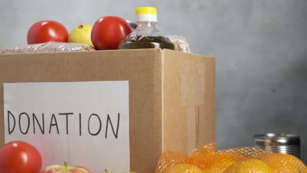 Donatie doos op tafel gevuld met levensmiddelen: groenten, olie, granen, fruit — Stockvideo