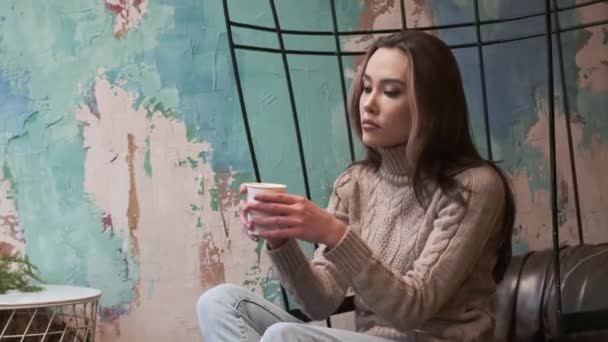 Fiatal ázsiai töprengő csinos lány ül hangulatos kávézó, iszik kofee reggel — Stock videók