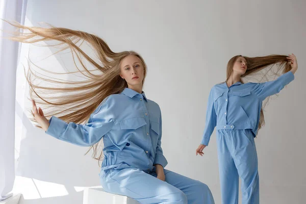 Duas jovens irmãs gêmeas bonitas com cabelo ondulado posando em ternos azuis em estúdio — Fotografia de Stock