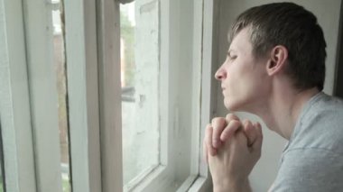 Camın arkasından bakan sıkılmış genç bir adam. Düşünceli erkek dışarı bakıyor.