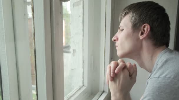 Verveelde jongeman die door het raam keek. attente man die naar buiten kijkt — Stockvideo