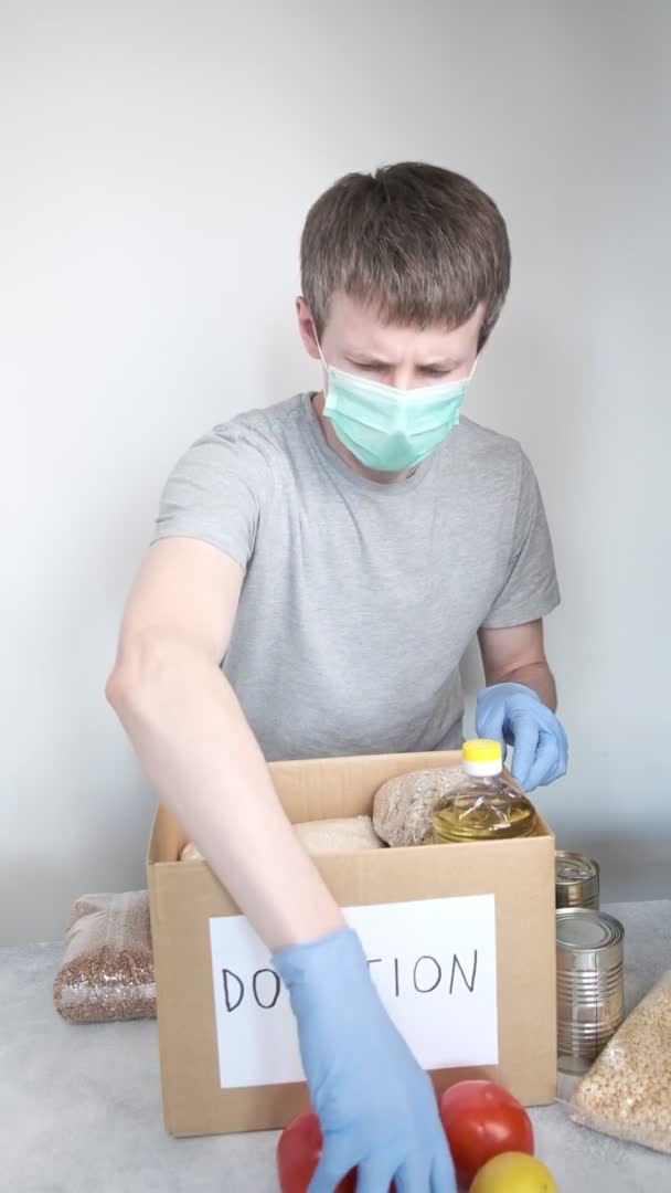 Εθελοντής σε μπλε προστατευτικά γάντια βάζοντας τρόφιμα παντοπωλείου στο κουτί δωρεάς χαρτοκιβωτίων — Αρχείο Βίντεο