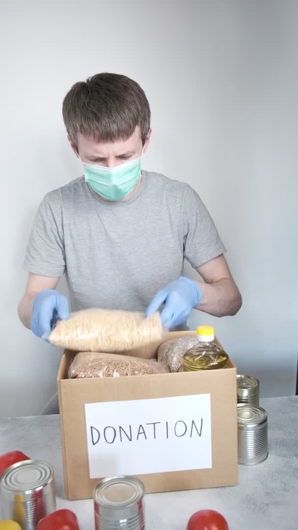 Волонтер в синіх захисних рукавичках покласти продуктову їжу в коробку для пожертвувань — стокове відео