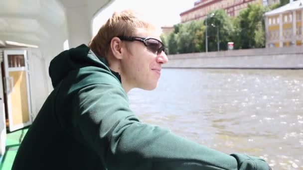 Mladý muž ve slunečních brýlích, usmívající se, plovoucí na řece Moskvě — Stock video