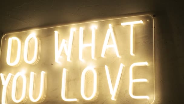 Der Titel macht, was man liebt, aus gelbem Neonlicht an der Wand. Festliche Dekoration — Stockvideo
