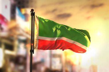Chechen Republic Flag Against City Blurred Background At Sunrise clipart