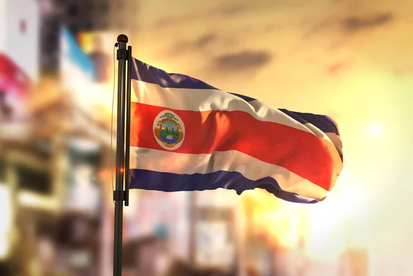 Bandeira de Costa Rica de encontro ao fundo borrado da cidade em Sunrise Backl — Fotografia de Stock