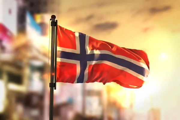 Norsko vlajka proti City rozmazané pozadí při východu slunce podsvícení — Stock fotografie
