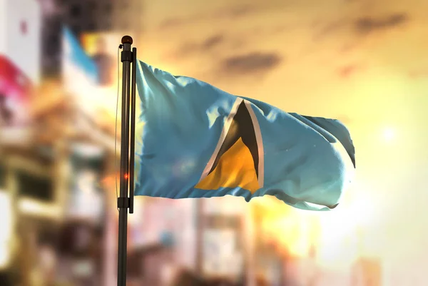 Saint Lucia flagę przed City niewyraźne tło o wschodzie słońca powrót — Zdjęcie stockowe