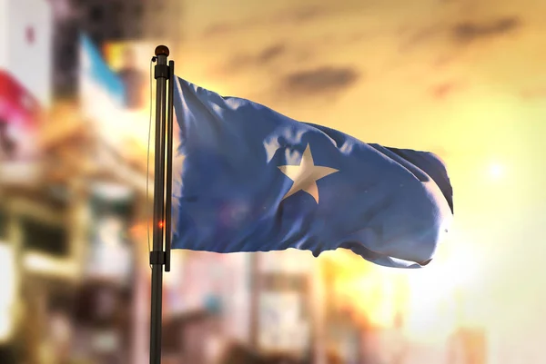 Somalia Flag Against City Blurred Background At Sunrise Backligh — Stock Photo, Image