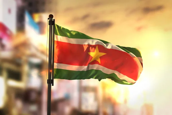 Suriname Flag Against City Blurred Background At Sunrise Backlig — Stock Photo, Image