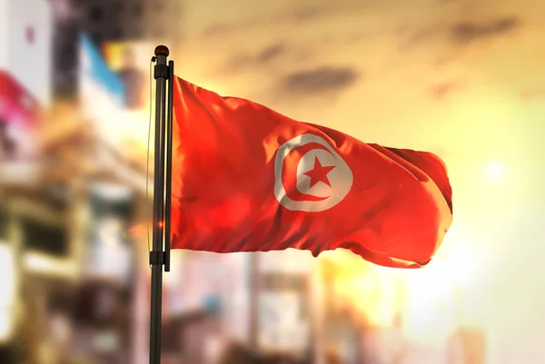 Tunesië vlag tegen stad wazig achtergrond bij zonsopgang Backligh — Stockfoto