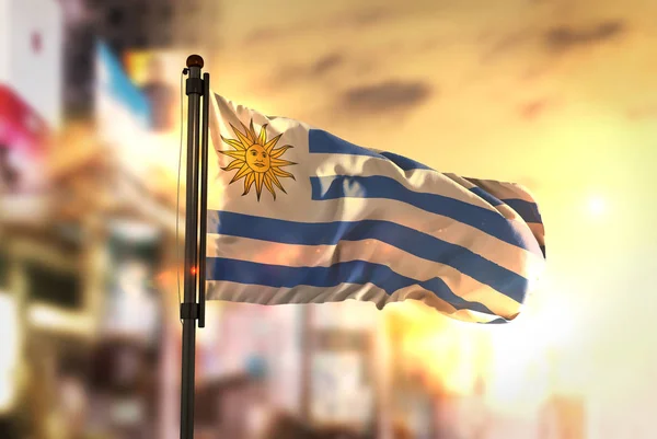 Uruguay vlag tegen stad wazig achtergrond bij zonsopgang Backligh — Stockfoto