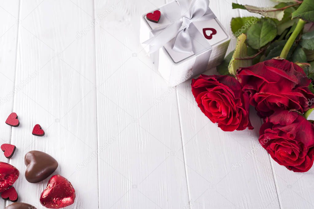 Valentines concept with bouquet of roses and wrapped gift on wooden table