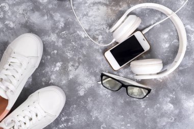 Düz yatıyordu, beyaz spor ayakkabı üzerinde taş arka plan ile telefon ve kulaklık.