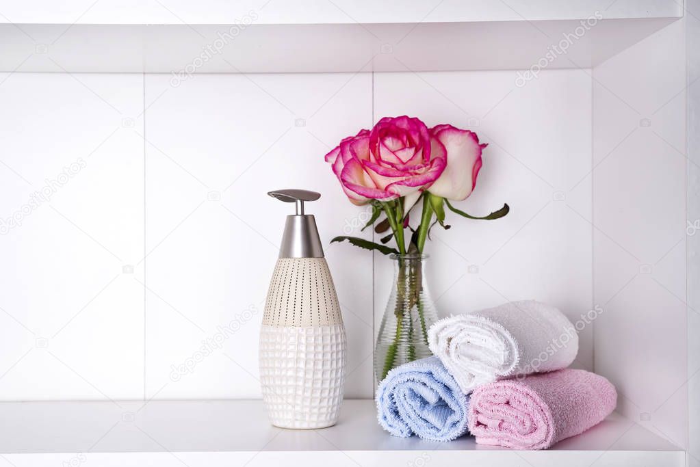 Stack of towels with a soap dispenser and roses in vasein a bathroom closeup