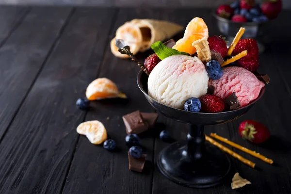 Bowl with ice cream with three different scoops of white, yellow, red colors and waffle cone, chocolate, tangerines and straws — Stock Photo, Image