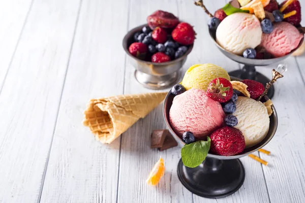 Cuenco con helado con tres cucharadas diferentes de blanco, amarillo, colores rojos y cono de gofre, chocolate, mandarinas y pajitas — Foto de Stock