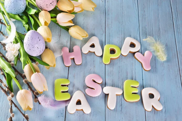 Easter cookies letter Happy Easter and colorful eggs with tulips on wood background