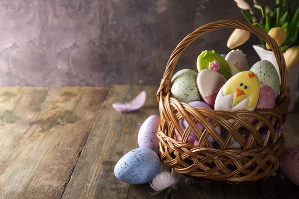 Uova pasquali colorate e biscotti in cesto e fiori di tulipani su tavolo di legno . — Foto Stock