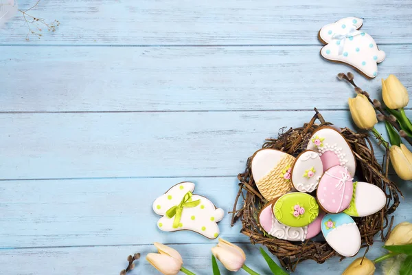 Schöne e Tulpen mit bunten Eiern im Nest und Plätzchen als Hase auf blauem Holzgrund — Stockfoto