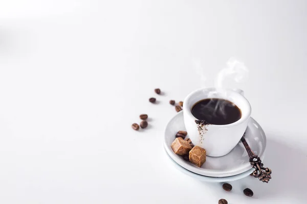 Kopp svart kaffe på ett tefat med brunt socker på en vit bakgrund — Stockfoto