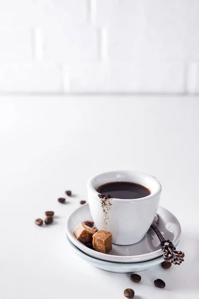 Kopp svart kaffe på ett tefat med brunt socker på en vit bakgrund — Stockfoto