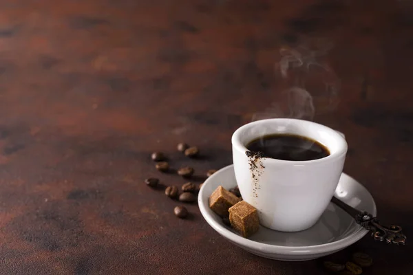 Kopje zwarte koffie op een schoteltje met bruine suiker op een steen bruin achtergrond — Stockfoto